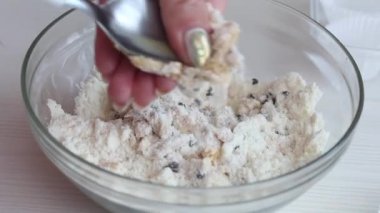 Bir kadın şeker yapmak için fıstık ezmesi, çikolata ve hindistan cevizi unu karıştırıyor. Masanın yanında kâğıt şekerli tartlar var. Yakın çekim..