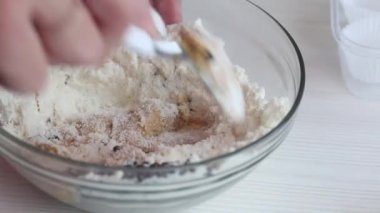 Bir kadın şeker yapmak için fıstık ezmesi, çikolata ve hindistan cevizi unu karıştırıyor. Yakınlarda kâğıt şekerli tartlar var. Yakın çekim.