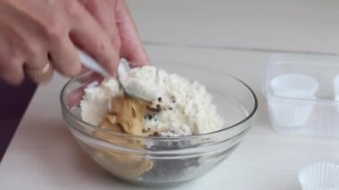 Bir kadın şeker yapmak için fıstık ezmesi, çikolata ve hindistan cevizi unu karıştırıyor. Yakınlarda kâğıt şekerli tartlar var. Yakın çekim..