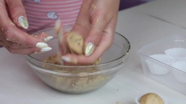 Une femme roule des boules de beurre d'arachide, de chocolat et de farine de noix de coco. Prépare des bonbons sains. Sur la table se trouvent des tartelettes en papier. Gros plan. — Video