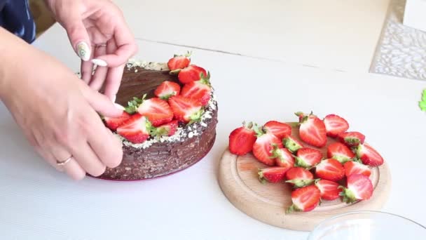 Una mujer decora un pastel con fresas. Cocinar pastel de chocolate con cacahuetes y fresas. Primer plano de disparo.. — Vídeo de stock