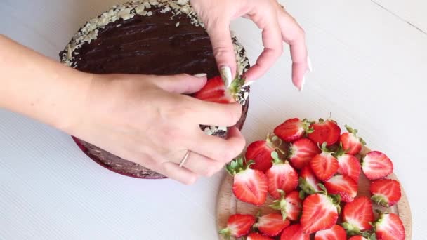 Una mujer decora un pastel con fresas. Cocinar pastel de chocolate con cacahuetes y fresas. Filmado desde arriba. — Vídeo de stock