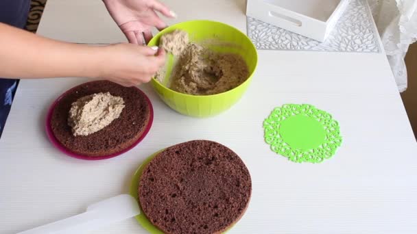 Eine Frau schmiert einen Keks-Kuchen mit Sahne. Schokoladenkuchen mit Erdnüssen und Erdbeeren kochen. — Stockvideo