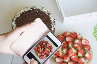 Kadın yemek pişirme sürecinin fotoğraflarını çekiyor. Fıstıklı ve çilekli çikolatalı pasta..