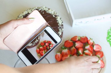 Kadın yemek pişirme sürecinin fotoğraflarını çekiyor. Fıstıklı ve çilekli çikolatalı pasta..