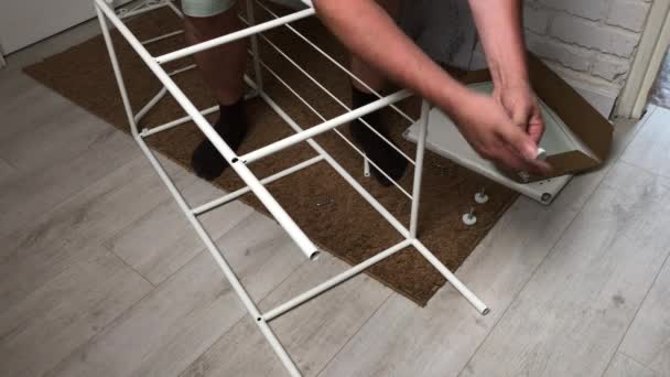 De man verzamelt het rek. Installeert de poten in de metalen plank. Huiswerk tijdens zelfisolatie. — Stockvideo
