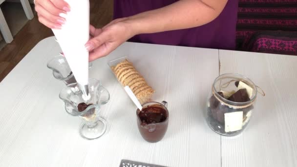 Eine Frau gibt Sahne aus einem Gebäckbeutel in ein Glas. Dessert mit Keksen, Schokolade und Sahne. — Stockvideo