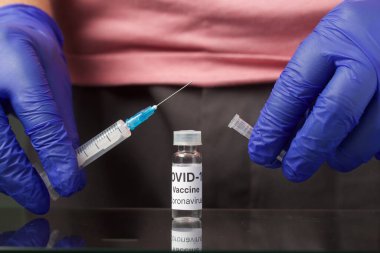 Koronavirüse karşı aşı. Ampulü aşıyla doldur. İğne için bir şırınganın ellerinde. Eldivenli eller. Yakın çekim..