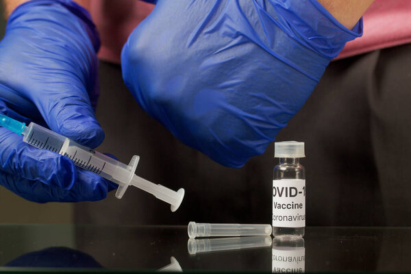 Vaccination against coronavirus. Ampoule with a vaccine. In the hands of a syringe for injection. Hands in rubber gloves. Close-up shot.