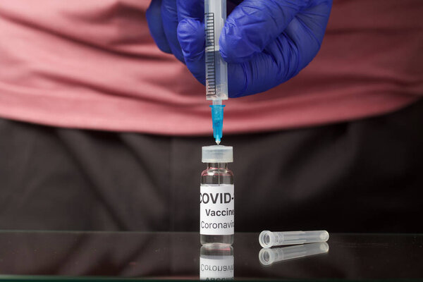 Vaccination against coronavirus. Ampoule with a vaccine. In the hands of a syringe for injection. Hands in rubber gloves. Close-up shot.