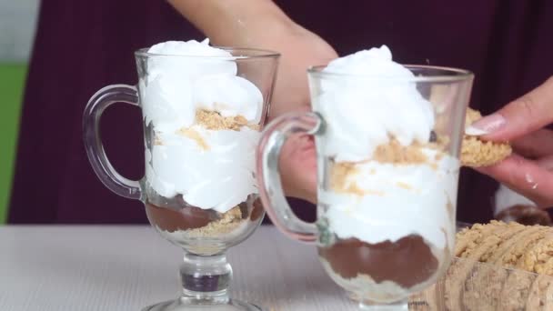 En kvinna tillagar en dessert av kex smulor, choklad och grädde. Dekorerar den med kakor. Närbild — Stockvideo