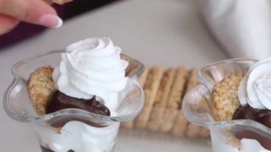 Kadın tatlıya bisküvi kırıntıları ekliyor. Bisküvi kırıntıları, çikolata ve kremadan tatlı hazırlar. Yakın çekim..