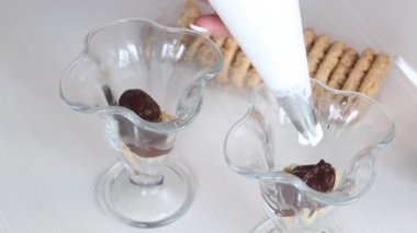 Bir kadın bisküvi ve çikolatalı tatlıya krema ekler. Yanında bisküvi ve çikolata var. Yakın çekim..