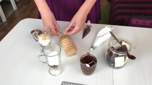 Una mujer añade migas de galletas a un postre con crema y chocolate. Galletas y chocolate cercanos. — Vídeo de stock