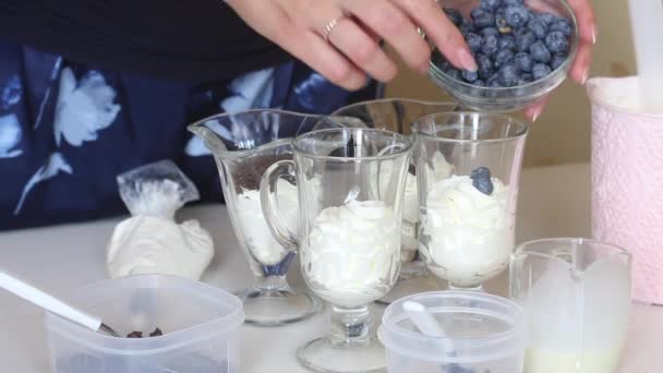 Seorang wanita menyiapkan hidangan penutup dengan krim kocok, blueberry dan cokelat. Hiasi makanan penutup dengan blueberry. — Stok Video