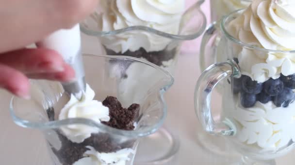 A woman prepares a dessert with whipped cream, blueberries and chocolate. Puts cream from a pastry bag. Close-up shot. — Stock Video