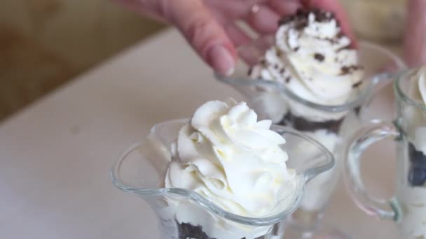 Een vrouw bereidt een toetje met slagroom, bosbessen en chocolade. Versiert het dessert met kruimels. Close-up opname. — Stockvideo