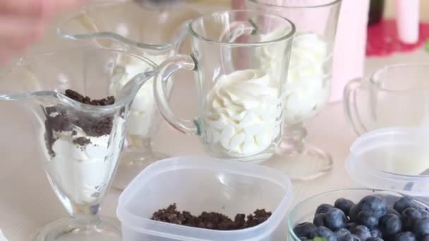 一个女人把巧克力滴在玻璃杯里的奶油上.附近有蓝莓和其他制作甜点的配料. — 图库视频影像