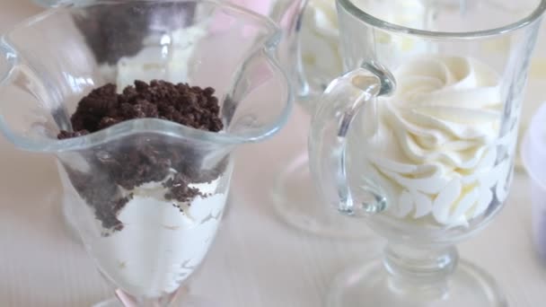 Egy nő desszertet készít tejszínhabbal, áfonyával és csokoládéval. A közelben csokoládé cseppek és egyéb összetevők a desszert. — Stock videók