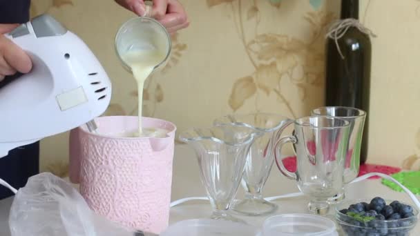 Bir kadın konteynırda krema ve konsantre süt deviriyor. Yakınlarda yabanmersini ve yoğunlaştırılmış süt var. Tatlı malzemeleri ekle — Stok video