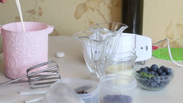 Una mujer vierte crema en un recipiente. Muy cerca están los arándanos y la leche condensada. Ingredientes de postre. — Vídeo de stock