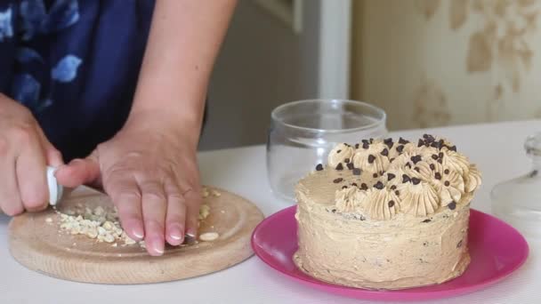 女性はピーナッツを研いでいる。その隣には、クリームとチョコレートドロップで装飾されたキャロットケーキです。クローズアップショット — ストック動画