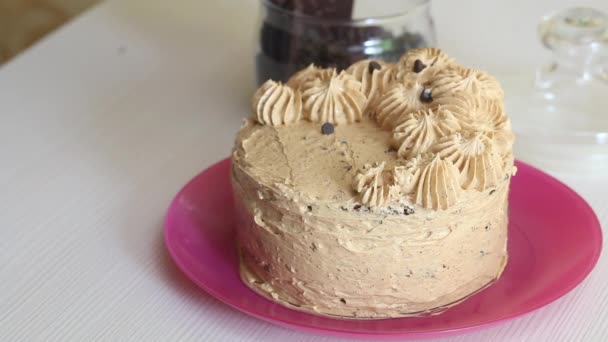 Eine Frau dekoriert einen Karottenkuchen mit Sahne und Schokolade. Daneben steht ein Glas mit Schokoladentropfen zur Dekoration. Nahaufnahme. — Stockvideo