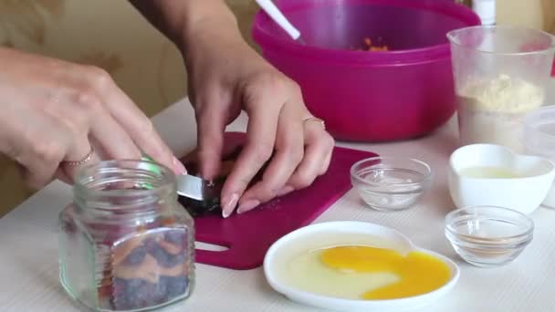 Cocinar pastel de zanahoria. La mujer corta frutas secas para el postre. Hay otros ingredientes para el pastel en la mesa cercana. — Vídeos de Stock