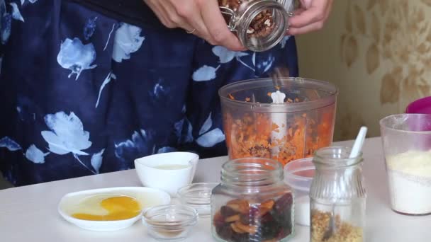 Worteltaart bakken. Een vrouw voegt een walnoot toe aan de blender kom. De ingrediënten worden op tafel gelegd. Close-up opname. — Stockvideo