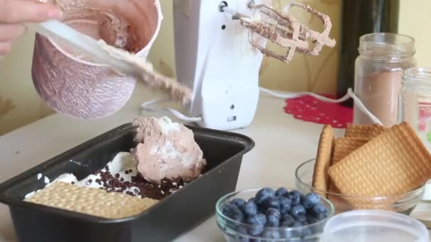 The woman adds a layer of chocolate cream to the container. Makes ice cream from cream, biscuits and crispbread. Other ingredients are spread out on the table nearby. Close-up shot. — Stockvideo