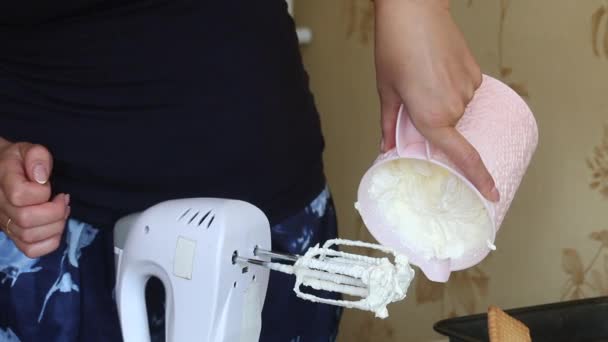 Une femme montre la crème fouettée dans un récipient. Fait de la crème glacée à partir de crème, biscuits et pain croustillant. D'autres ingrédients sont répartis sur la table à proximité. — Video