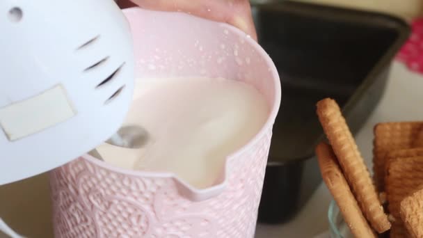 A woman is whipping cream in a container. Makes ice cream from cream, biscuits and crispbread. The ingredients are located next to each other on the table. Close-up shot — Stock Video