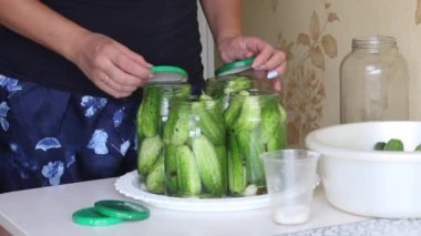 Kadın salatalık kavanozunun kapağını kapatıyor. Salatalıklar salamura ile kaplıdır. Hasat koruma.