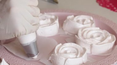 Kadın lokum lalelerini şekillendiriyor. Hortumlu bir hamur torbasıyla. Tepsinin üzerinde marşmelov gülleri var. Yakın çekim..