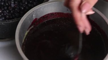 Bir kadın lavanta tozu ve yaban mersini püresini kaşıkla karıştırıyor. Evde lavantalı yaban mersini reçeli yapıyorum. Yabanmersinlerinin korunması ve hazırlanması. Yakın çekim..