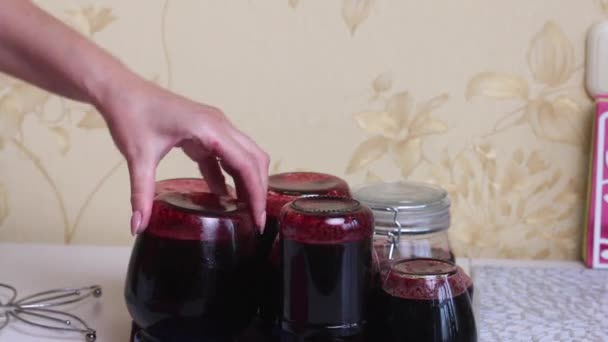 Kobieta prostuje wywrócone słoiki dżemu jagodowego na stole. Robię dżem jagodowy w domu. Konserwacja i przygotowanie jagód. — Wideo stockowe