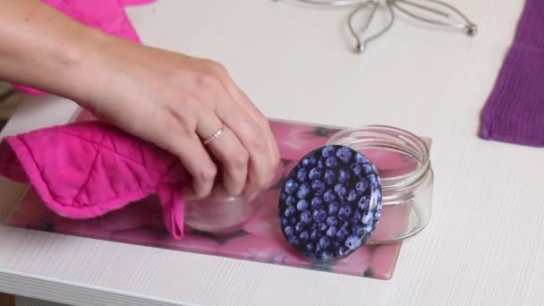 La femme met des bocaux stérilisés chauds sur la table. Pour la confiture de myrtilles. Faire de la confiture de myrtilles à la maison. Conservation et préparation des bleuets. — Video