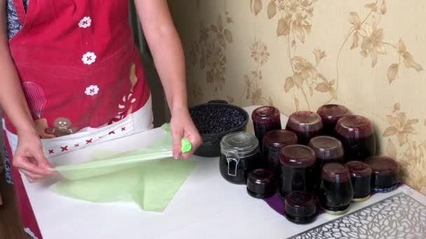 Kobieta przygotowuje torby na mrożone jagody. Świeżo zrobiony dżem jagodowy w pobliskich słoikach. Konserwacja i przygotowanie jagód. — Wideo stockowe