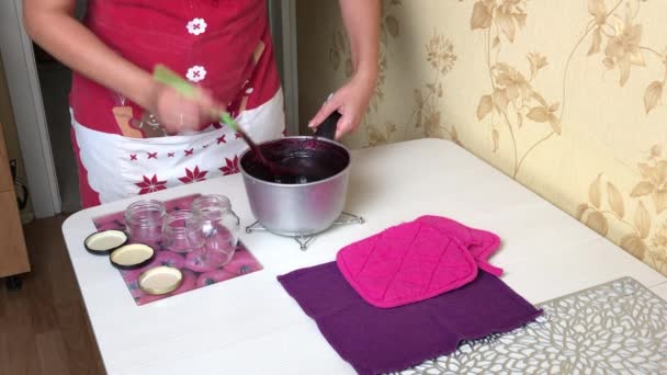 En kvinde hælder kogt blåbærsyltetøj i krukker. Laver blåbærsyltetøj derhjemme. Bevarelse og tilberedning af blåbær. – Stock-video