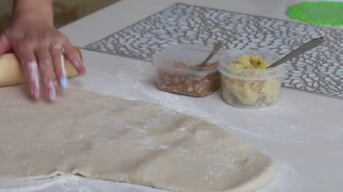 Bir kadın hamur işi için hamur topluyor. Yakınlarda patatesli kaplar ve dolgu için kıyma var. Yakın çekim..