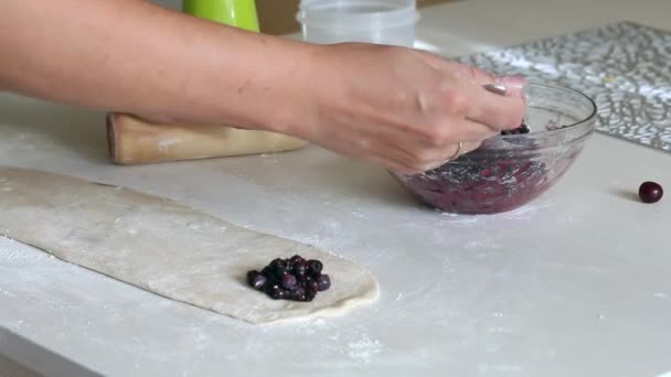 Uma mulher prepara bolinhos com mirtilos. Lugares mirtilos na massa de farinha enrolada. Mirtilos nas proximidades em um recipiente. — Vídeo de Stock