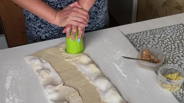 Een vrouw wikkelt aardappelpuree en gehakt in gerold deeg. Vormt knoedels met een plastic glas. Kookdumplings gevuld met aardappelpuree en gehakt vlees — Stockvideo