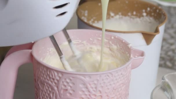 Eine Frau schlägt Sahne mit dem Mixer. Gleichzeitig gibt er ihnen Kondensmilch hinzu. Bereitet Sahne für das Dessert zu. Dessert mit Sahne und Kekskrümeln. Nahaufnahme — Stockvideo