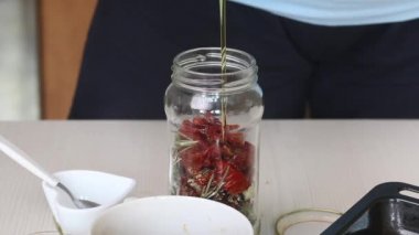 Bir kadın zeytinyağlı kavanoza baharat ve kurutulmuş domates koyar. Zeytinyağında güneşte kurutulmuş domates pişiriyorum. Yakın çekim..