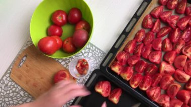 Kadın domatesleri bir kesim tahtasıyla kesiyor ve onları pişirme tepsisine koyuyor. Zeytinyağında güneşte kurutulmuş domates pişiriyorum. Yukarıdan çekilen.