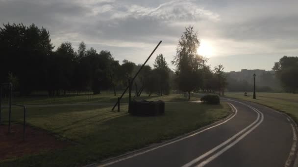 公园里一条蜿蜒的自行车道 它蜿蜒穿过树林和灌木丛 黎明时拍摄 日出时拍摄 升起的太阳的光芒是可见的 空中摄影 — 图库视频影像