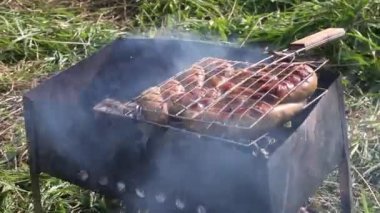 Kahverengi sosisli ızgara rafı. Közlerle ızgarada yatıyor. Çayırda, yeşil çimlerin arasında. Doğada piknik. Yakın çekim.