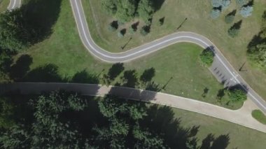 Şehir parkında uçuş. Aşağıda virajlı bisiklet yolu görülebilir. Güçlü bir rüzgar ağaçları sallıyor. Hava fotoğrafçılığı.