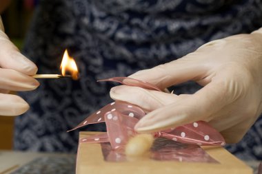 Bir kadın el işi ambalajında şekerleme paketliyor. Bandı kibritle dağlıyor. Yakınlarda marşmelov gülleri ve laleler var. Yakın çekim..