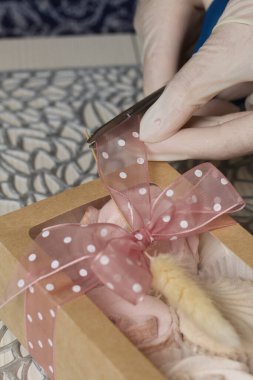 Bir kadın ev yapımı marşmelov paketini kurdele ve lagurularla süslüyor. Yakınlarda marşmelov gülleri ve laleler var. Yakın çekim..